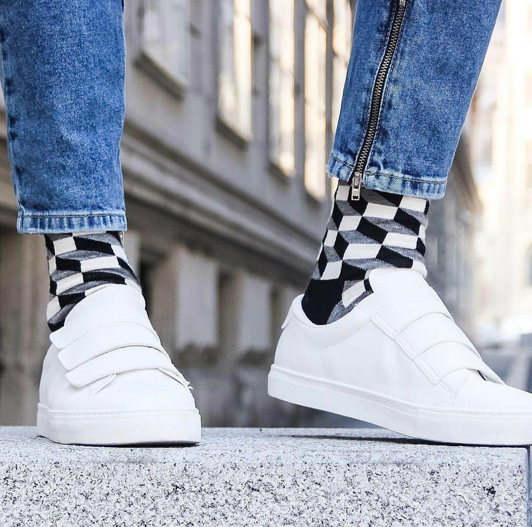 A person wearing white sneakers and blue jeans, with checkered socks peeking out from the jeans.